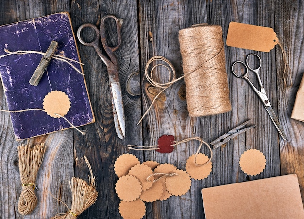 Bobine de corde marron, étiquettes en papier et vieux ciseaux sur bois gris