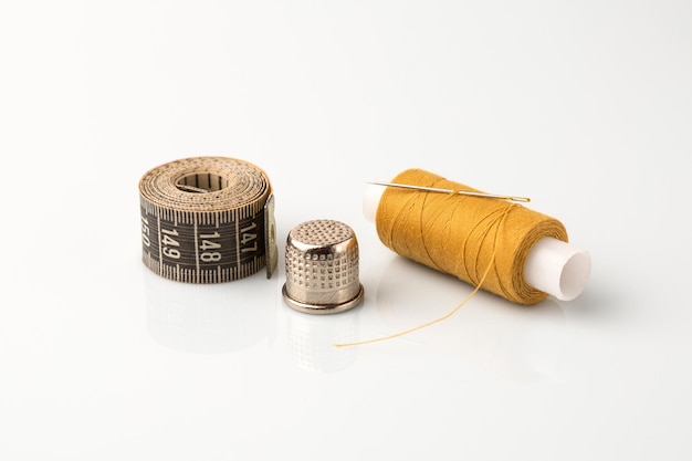 Photo bobine de fil jaune avec un dé à coudre et un ruban à mesurer sur fond blanc.