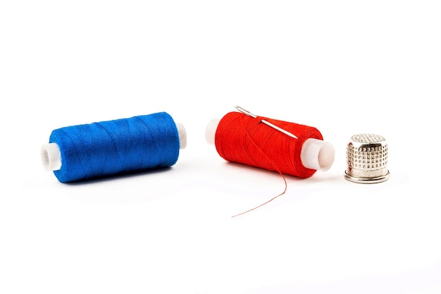 Une bobine de fils bleus et rouges avec une aiguille et un dé à coudre sur un fond blanc isolé