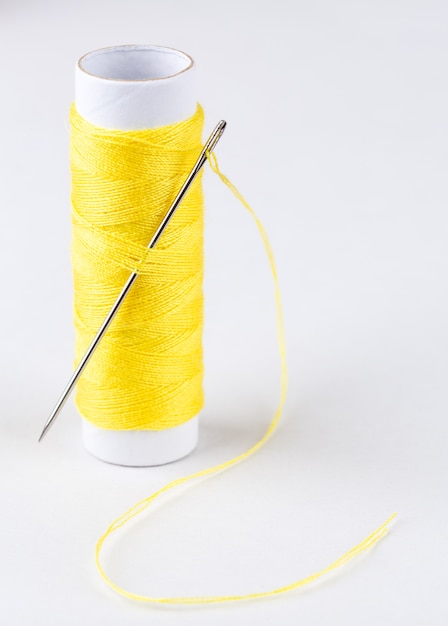 Photo bobine de fils jaunes et une aiguille sur fond blanc
