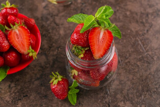 Un bocal en verre de fraises juteuses rouges sur table marron foncé