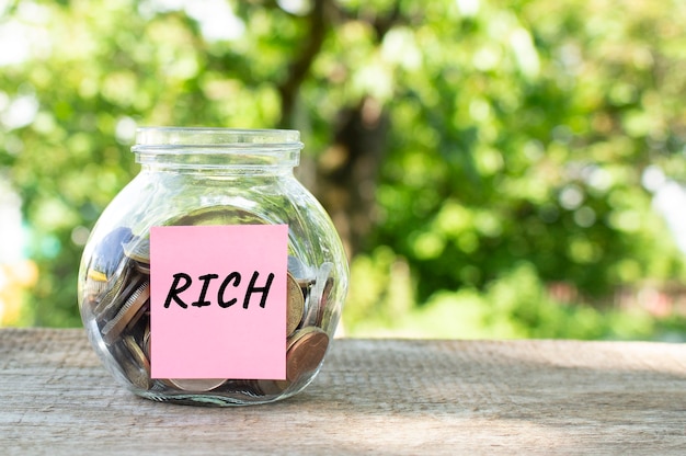 Un bocal en verre avec des pièces de monnaie et l'inscription RICH sur une table en bois. Budget pour investir.