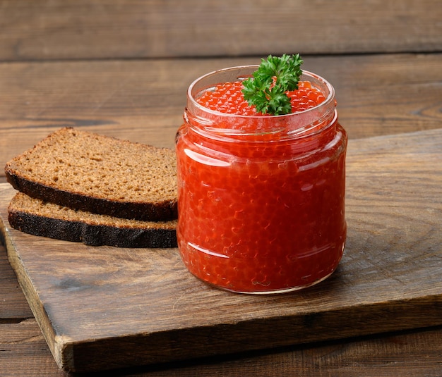 Bocal en verre plein avec du caviar rouge sur une table en bois marron, petit déjeuner