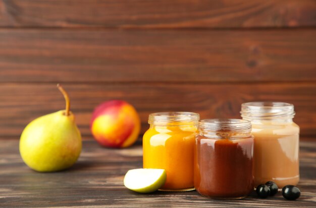 Bocaux en verre avec des aliments pour bébés et des fruits sur brown