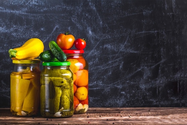 Bocaux En Verre De Concombres Frais Marinés, Courgettes Et Tomates Sur Un Fond Sombre. Espace De Copie. Stock De Nourriture