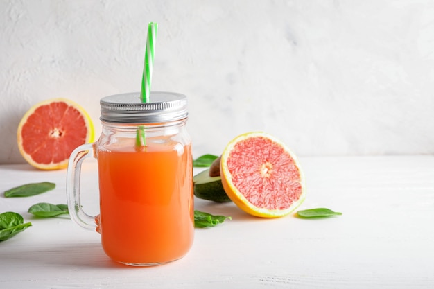 Bocaux en verre avec du jus de pamplemousse frais et des pamplemousses mûrs sur fond blanc.