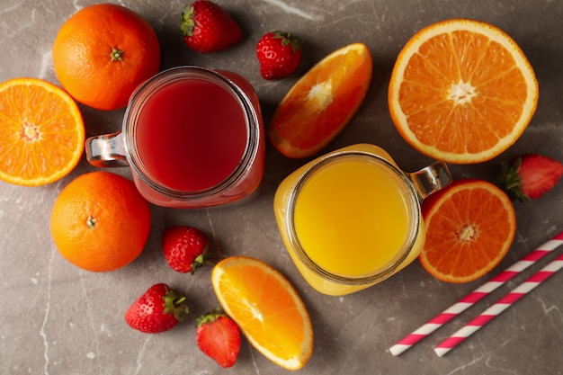 Bocaux en verre avec jus de fraise et d'orange sur fond gris