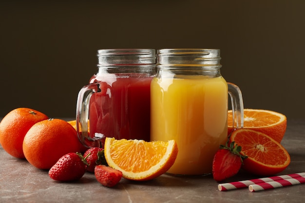 Bocaux en verre avec jus de fraise et d'orange sur fond gris