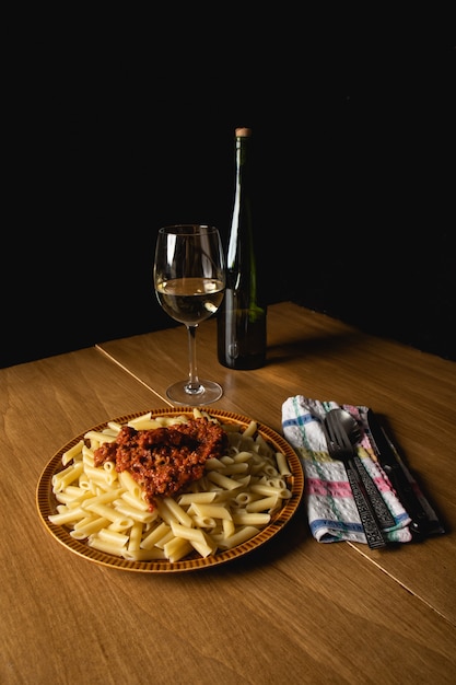 Bodegon de plat de macaronis avec sauce bolognaise et fromage râpé et un verre de vin d&#39;accompagnement.