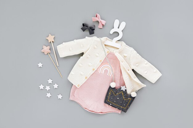 Photo body rose avec pull en tricot, sac à main pour enfants en forme de couronne sur un joli cintre avec des oreilles de lapin. ensemble de vêtements et accessoires pour bébé sur fond gris. tenue de mode pour enfants. mise à plat, vue de dessus