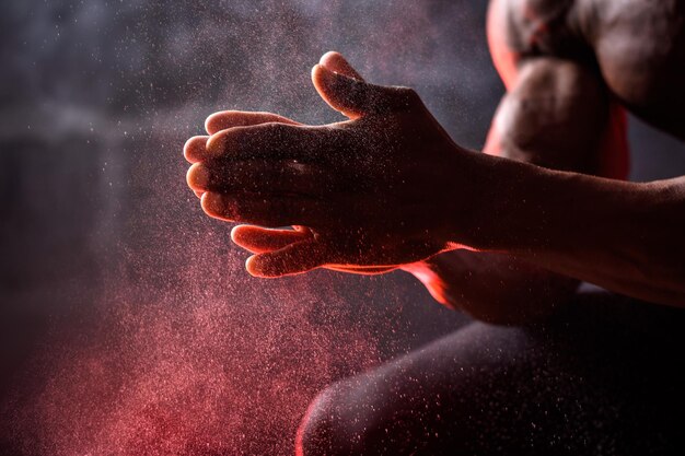 Bodybuilder afro-américain utilise de la magnésie à la main. Un homme est assis sur un fond noir avec de la fumée rouge