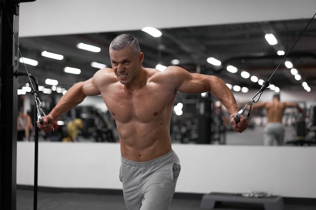 Bodybuilder athlétique musculaire debout formation des muscles de la poitrine et des épaules sur l'équipement de fitness