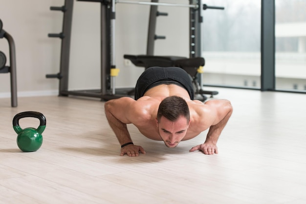 Bodybuilder faisant des pompes sur le sol avec Kettlebell