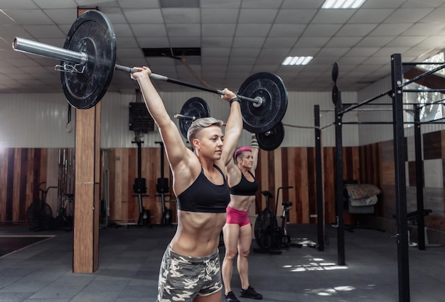 Bodybuilder de femmes fortes faisant des frais généraux avec des haltères lourds dans une salle de sport croisée moderne. Cours d'entraînement fonctionnel. Musculation et remise en forme