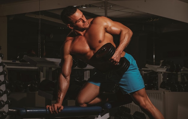 Bodybuilder formation biceps dans la salle de gym soulevant des haltères Exercices et entraînement Sportif avec torse torse nu