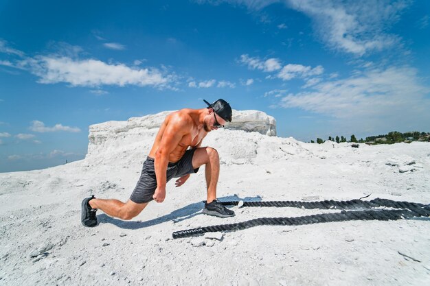 Bodybuilder fort brutal posant en plein air Séance photo dans une carrière Concept de sports de plein air Posant avec des cordes Paysage blanc