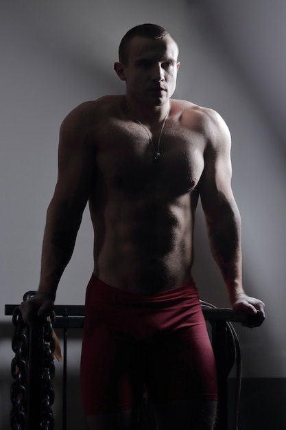 Bodybuilder masculin élégant avec une chaîne lourde debout dans la salle de gym.