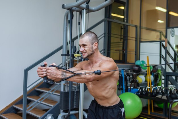 Bodybuilder musculaire avec des exercices de torse nu dans une machine de croisement de câbles. Hommes de remise en forme pompant les muscles dans la salle de gym.