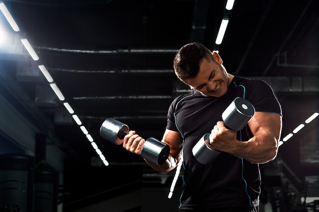 Bodybuilder musculaire, faire des exercices avec haltère dans la salle de gym. Homme athlétique fort montre le corps, les muscles abdominaux, les biceps et les triceps.Travaillez, prenez du poids, gonflez vos muscles avec des haltères.