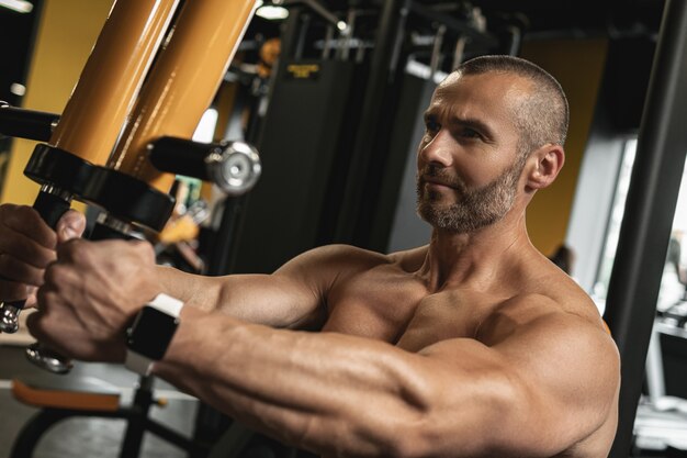 Bodybuilder musculaire faisant de l'exercice pec deck pour une poitrine pendant son entraînement dans la salle de gym