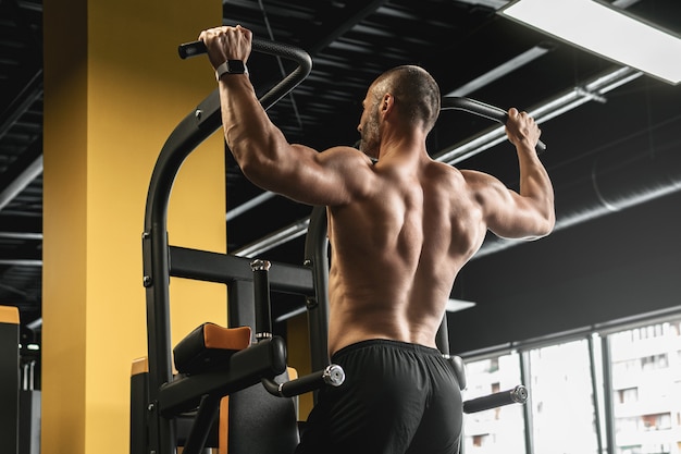 Bodybuilder musculaire faisant des tractions pendant son entraînement dans la salle de gym