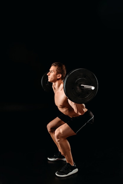 Bodybuilder sexy avec torse musclé accroupi avec haltères isolé sur noir