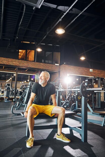 Bodybuilder à tête grise barbu souriant joyeux regardant loin