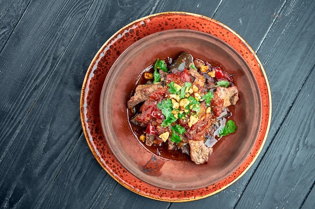 Boeuf au four avec aubergines, noix, tomates et coriandre en argile, servi dans un bol sur une surface noire. Nourriture de restaurant.