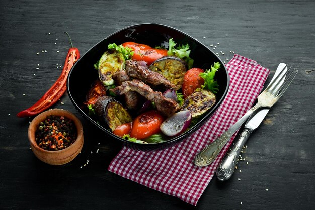 Bœuf cuit au four et légumes grillés dans une assiette noire Sur un fond en bois Vue de dessus Espace libre pour votre texte