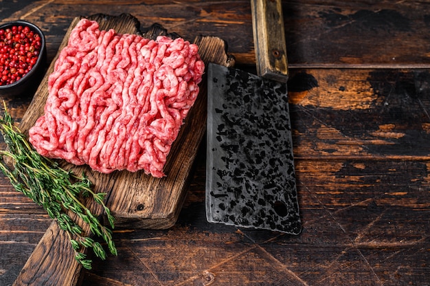 Boeuf haché cru, viande hachée aux herbes et épices sur une planche à découper en bois. Fond en bois sombre. Vue de dessus. Espace de copie.