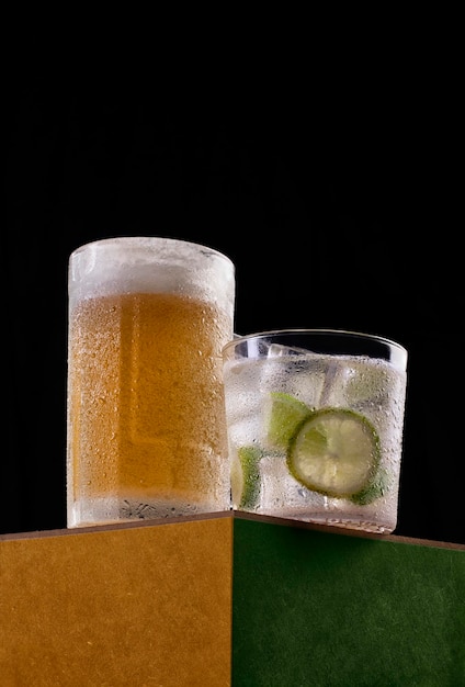 Boire de la caipirinha brésilienne à côté d'un verre de bière en photo haute résolution en studio avec un fond noir aux couleurs vertes et jaunes