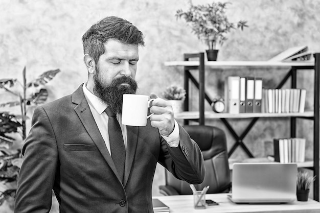 Boire du café pause détente Patron profitant d'une boisson énergisante Commencez la journée avec du café Les gens qui réussissent boivent du café Accro à la caféine Homme barbu homme d'affaires tenir une tasse de café debout fond de bureau