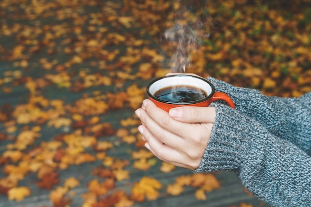 Boire du thé ou du café d'automne dans les mains sur fond de feuilles jaunes d'octobre confort d'automne et mo...