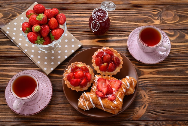 Boire du thé avec des tartelettes et des gâteaux aux fraises