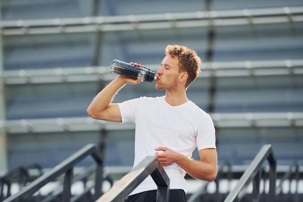 Boire de l'eau et faire une pause Jeune homme en vêtements de sport s'entraîner à l'extérieur pendant la journée