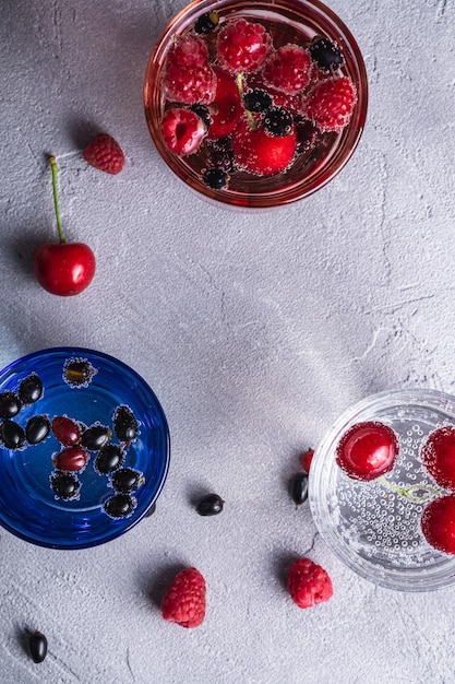 Boire de l'eau gazeuse fraîche avec des baies de cerise, de framboise et de cassis dans trois verres colorés sur pierre