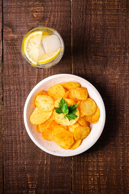 Boire de l'eau glacée fraîche avec du citron près de chips de pommes de terre frites ondulées dorées