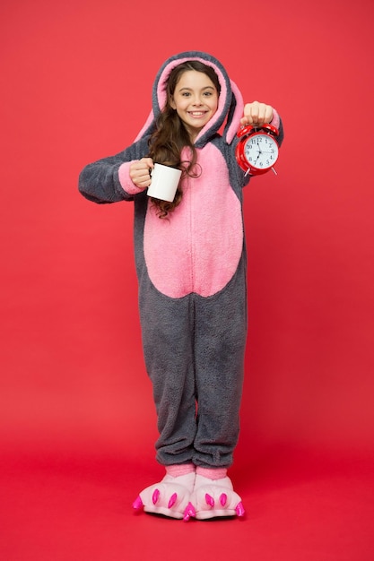 Boire de l'énergie du café Lapin enfant fond rouge Bébé animal Compter le temps Routines du matin Adorable lapin tenir réveil Petite fille en costume de lapin Enfant lapin kigurumi Pyjama fille lapin