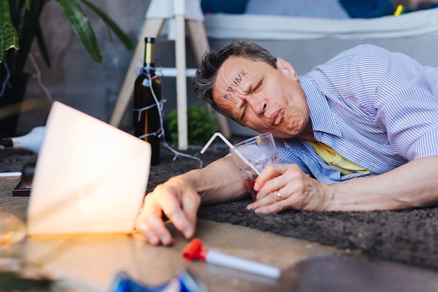 Boire nocive. Homme mature fatigué localisant sur le sol et avaler un cocktail