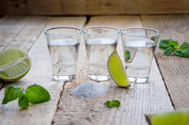 Boisson alcoolisée. Tequila en argent avec citron vert, sel et vert sur la table en bois