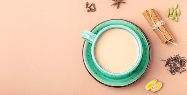 Boisson au thé indien avec du lait et des épices dans une tasse de thé verte rustique avec des ingrédients pour faire du masala chai