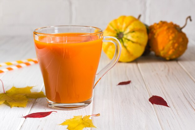 Boisson d'automne traditionnelle. Tasses en verre de jus de citrouille, citrouilles et feuilles d'érable tombées