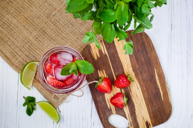 Boisson aux fraises dans un verre au citron vert et menthe sur un fond en bois