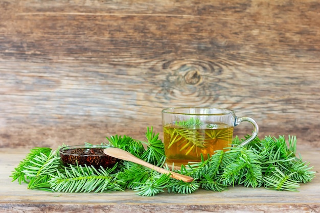 Une boisson à base d'aiguilles de pin dans une tasse avec des aiguilles de sapin vert et de la confiture de pommes de pin sur un fond en bois avec un espace de copie en gros plan