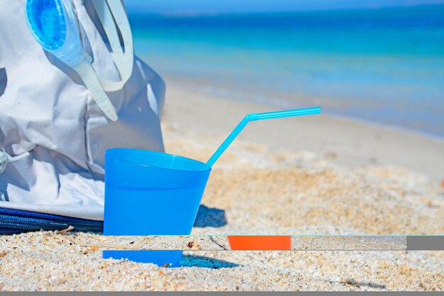 Boisson bleue et sac de plage sur un rivage blanc