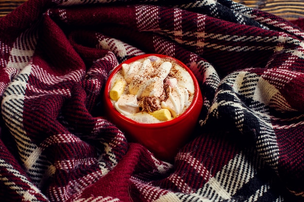 Boisson café en hiver, cacao à la crème fouettée et guimauves dans une tasse en céramique rouge