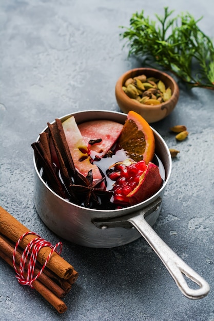 Boisson chaude au vin chaud aux agrumes, pomme, grenade et épices dans une cocotte en aluminium avec des jouets d'arbre de Noël vintage et une branche de sapin sur une surface en béton. Mise au point sélective.