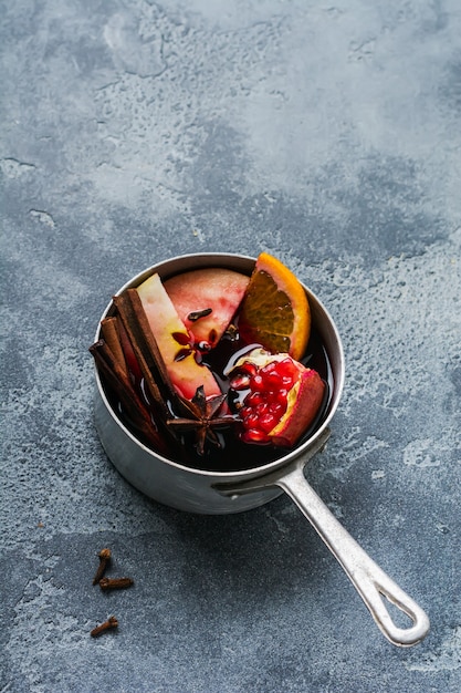 Boisson chaude au vin chaud aux agrumes, pomme, grenade et épices dans une cocotte en aluminium avec des jouets d'arbre de Noël vintage et une branche de sapin sur une surface en béton. Mise au point sélective.