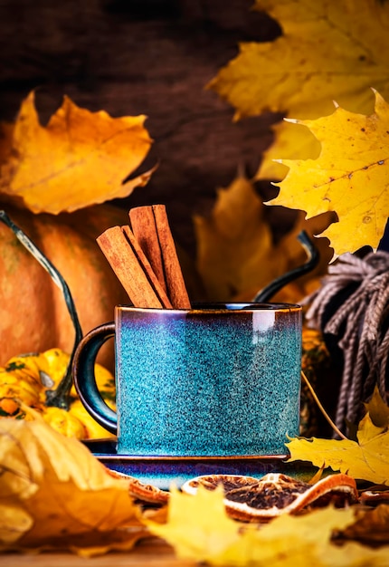 Boisson chaude d'automne dans une tasse bleue sur fond d'automne avec des citrouilles, des feuilles tombées, des vêtements d'automne, des écharpes sur une table en bois rustique