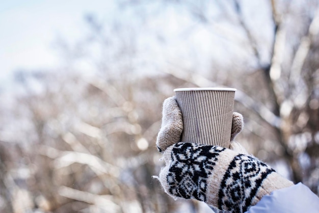 Boisson chaude dans les mains d'une femme portant des gants tricotés chauds par temps froid d'hiver enneigé.